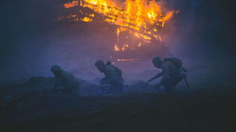 Soldiers sneak silently past the fiery wreckage of a weapon of war now immobile.