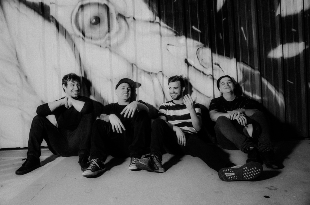 Emo Music band Sleep Eater's band members sit by a wall of graffiti.